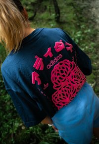 Mørkeblå bomulds T-shirt med stort pink grafisk design, der viser japanske tegn og blomster mønstre på ryggen. Korte ærmer.