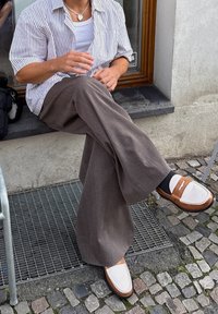 Volné hnědé kalhoty s texturovaným povrchem, zkombinované s pruhovanou košilí s krátkým rukávem a dvoubarevnými mokasíny s bílým akcentem.