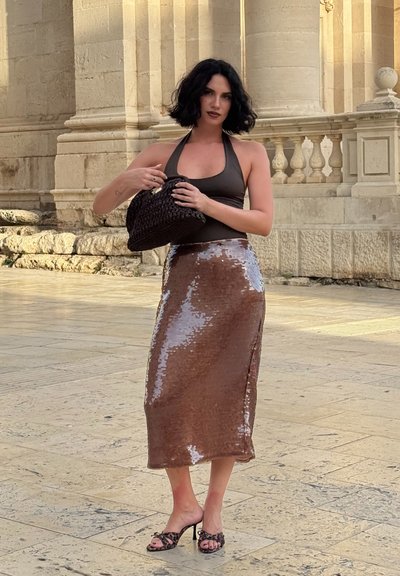 Falda midi de lentejuelas marrón con un acabado brillante, combinada con un top negro sin mangas y un bolso de mano tejido negro. Unas sandalias negras de tacón completan el look.