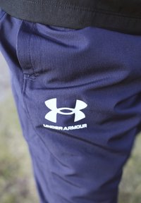 Navy athletic trousers with a ribbed texture, featuring a white Under Armour logo on the side and an elasticated waistband.