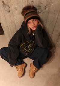 Felpa nera oversize con grafiche gialle, jeans blu scuro e stivali beige con lacci gialli e suole marroni. Berretto a righe marroni.