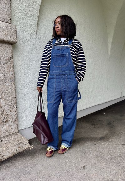 Pantalones de mezclilla en azul, camiseta de rayas de manga larga en blanco y negro, combinados con un bolso burdeos y zapatos multicolores. Fondo de pared texturizada.