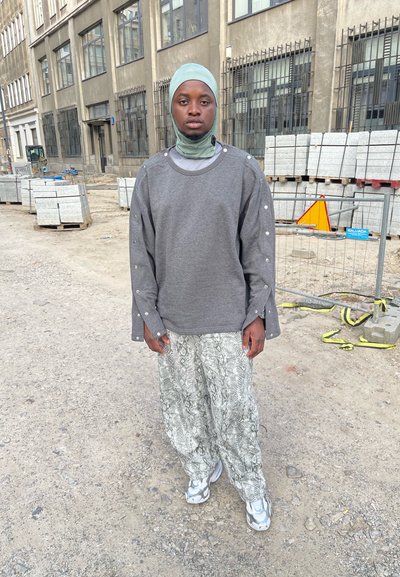 Sudadera gris de gran tamaño con mangas largas que presenta detalles de botones a presión plateados, combinada con pantalones de patrón de serpiente gris claro y zapatillas plateadas.