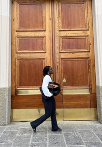 En person går forbi store, doble, tre dører med messingbelagte sparkplater, holder en svart veske, iført hvit genser og svarte bukser.