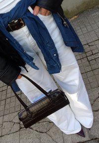 Sac à main noir à texture crocodile avec poignées courtes, porté avec un pantalon blanc à jambes larges et une chemise en jean bleue par-dessus un haut blanc.