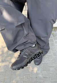 Črne športne čevlje z teksturiranim mrežastim zgornjim delom, detajlom treh črt in značilno debelo podplatom z okroglimi izrezi.