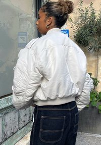 White bomber jacket featuring a quilted texture and ribbed hem, teamed with dark blue denim jeans. The pockets have visible stitching.