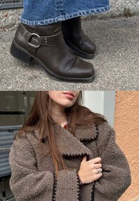 Botines de cuero marrón con punta redondeada y hebilla decorativa. Abrigo de piel marrón acogedor con ribete negro contrastante y corte holgado.