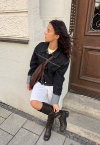 Črna denim jakna z sivimi manšetami, bele kratke hlače in rjavi usnjeni čevlji do kolen. Rjava torbica čez ramo in oblikovani valoviti lasje.