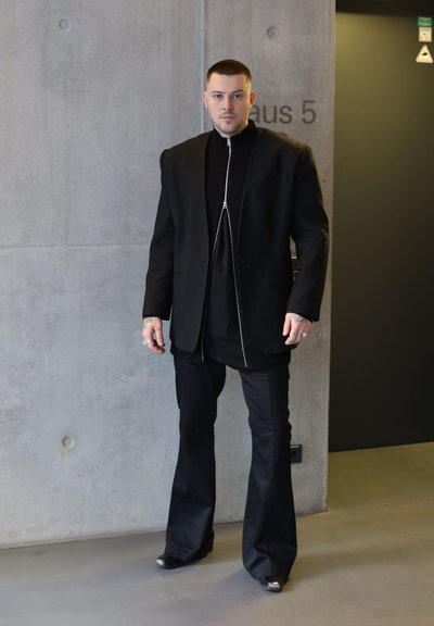 Blazer negro de gran tamaño sobre una camiseta de cremallera negra acanalada, combinado con pantalones negros de campana y calzado con acentos metálicos. Textura suave, diseño minimalista.