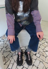 Langærmet skjorte med grafisk print og ternede manchetter, kombineret med blå denimjeans og sorte sneakers med pink snørebånd. Grå sokker er synlige.