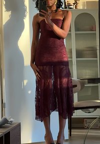 Μπορντό δαντελένιο φόρεμα με εφαρμοστό κολλητό τοπ χωρίς τιράντες και διαφανή, ρέουσα φούστα. Ο σχεδιασμός διαθέτει μήκος μέχρι το γόνατο και περίπλοκα λουλουδάτα μοτίβα.