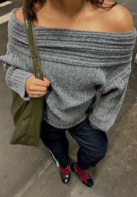Grey off-the-shoulder jumper with ribbed texture, green shoulder bag, dark jeans, and black patent leather shoes with maroon socks.