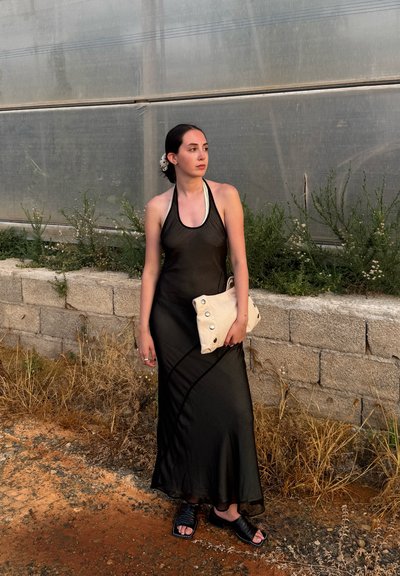 Vestido negro sin mangas con un diseño fluido, combinado con un clutch de color claro con acentos de botones y sandalias negras de deslizamiento.