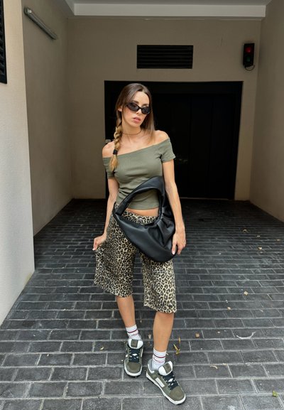 Top ajustado verde oliva sin hombros, culottes de print leopardo beige, bolso hobo negro y zapatillas grises con acentos blancos sobre un pavimento texturizado.