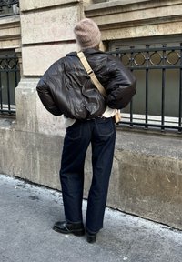 Καφέ παλτό με επένδυση σε υπερμεγέθη εφαρμογή, λευκό πουλόβερ, σκούρα μπλε τζιν και μαύρα παπούτσια. Τα αξεσουάρ περιλαμβάνουν μια ανοιχτόχρωμη τσάντα και κασκόλ.