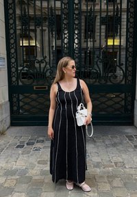 Μαύρο maxi φόρεμα με λευκές κατακόρυφες ρίγες, φορεμένο με μια μικρή λευκή τσάντα. Διαθέτει στρογγυλή λαιμόκοψη και ανοιχτόχρωμα μπεζ σανδάλια.