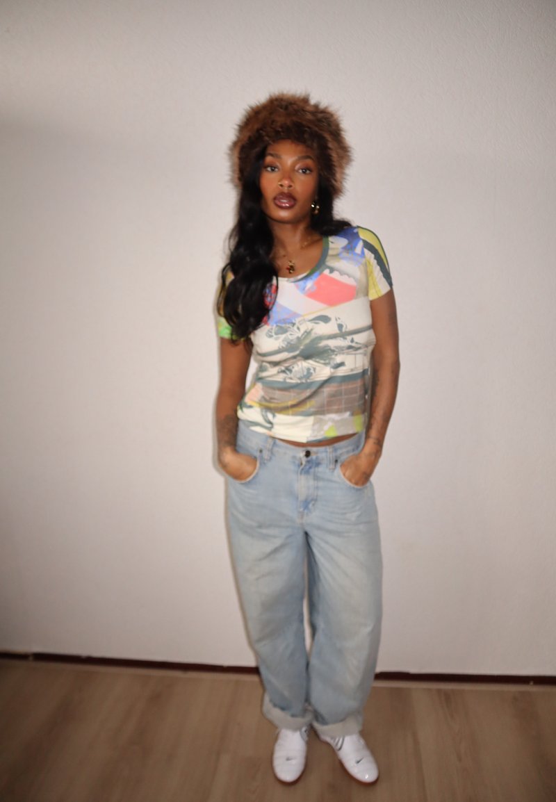Maglietta a maniche corte con grafica multicolore abbinata a jeans larghi azzurro chiaro. Scarpe da ginnastica bianche e cappello di pelliccia marrone completano il look.