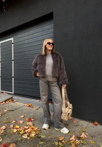 Faux pels grå cropped jakke over en lys grå genser, parret med vide grå bukser og hvite joggesko, holder en beigefarget stoffhåndveske.