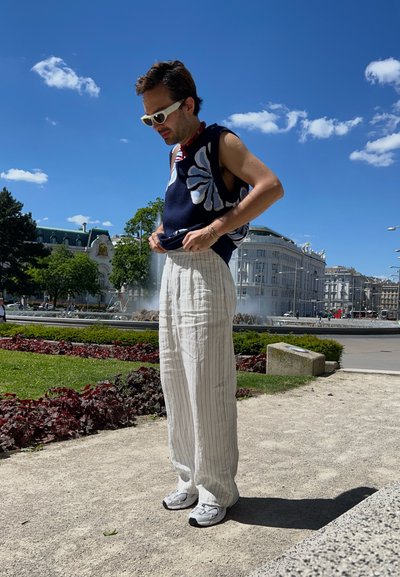 Top sin mangas en color navy con un estampado floral, pantalones de pierna ancha a rayas blancas y zapatillas grises; unas gafas de sol complementan el atuendo casual.
