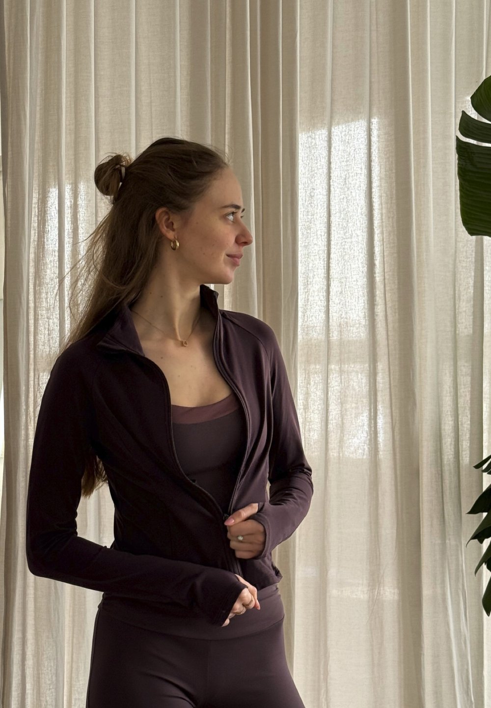 Jachetă sportivă mov închis, cu design strâmt și guler înalt, combinată cu un maiou și colanți asortați. Material neted și elastic.