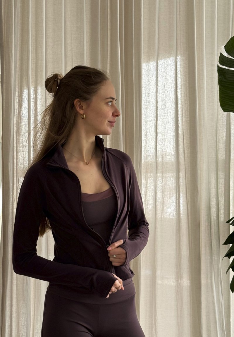 Dark purple athletic jacket with a fitted design and high collar, paired with a matching tank top and leggings. Smooth, stretchy fabric.