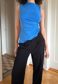 Haut bleu sans manches avec détail froncé sur le côté, assorti à un pantalon noir ample. Tissu lisse ; le haut est coupé de manière asymétrique à l'ourlet.