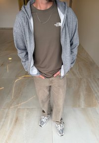 Grå zip-up hoodie over en olivengrøn t-shirt, parret med tan corduroy bukser og grå sneakers. Sølv kædehalskæde synligt.