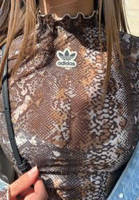 Καφέ και μπεζ τοπ με σχέδιο φίδι και κομμένες άκρες στον λαιμό, διαθέτοντας λογότυπο Adidas. Περιλαμβάνει μαύρη ζώνη και υφασμάτινη υφή.