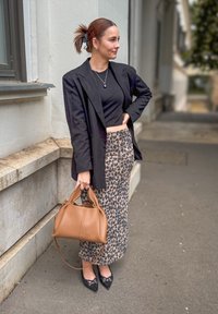 Μαύρο σακάκι, κοντή μαύρη μπλούζα, φούστα με λεοπάρ τυπωμένο σχέδιο, καφέ τσάντα, μυτερές μαύρες γόβες με λεπτομέρειες; εξωτερικός αστικός χώρος.