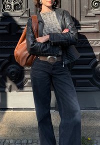 Zwarte leren jack met gewatteerde details, grijs geruite top, ruime zwarte jeans, tan leren schoudertas, zilveren ceintuursluiting, grote oorbellen.
