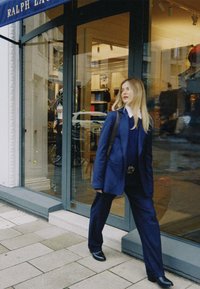 Ναυτικό κοστούμι με υπερμεγέθη σακάκι και ραμμένο παντελόνι. Συνδυασμένο με μαύρα παπούτσια. Η βιτρίνα με γυάλινη πόρτα εμφανίζει ρούχα στο εσωτερικό.