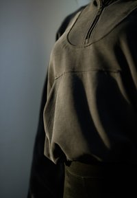 Dark grey zip-up top featuring textured fabric, ribbed accents, and a rounded neckline, paired with a smooth, fitted lower section.