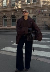 Mørkebrun oversized lærjakke, brun genser, høy midje mørk denim flared bukser, svarte hansker, stor mørk håndveske og oversized solbriller.