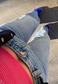 Jeans in denim blu chiaro a gamba larga con bottoni color rame, abbinati a un top rosa a costine e scarpe blu, ripresi da un basso angolo.