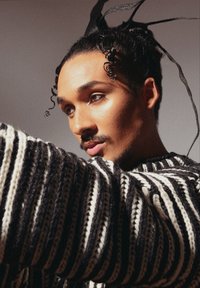 Pull en maille épaisse à rayures noir et blanc, présentant un motif texturé. Le modèle a des cheveux bouclés avec des rubans, mettant en valeur un gros plan de son profil.