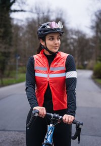 Gilet da ciclismo rosso con bande riflettenti, indossato sopra una maglietta a maniche lunghe nera. Ciclista su una bicicletta blu con casco nero e occhiali.