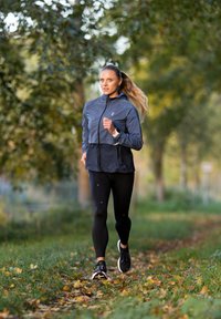 Spordijakk tumesinisena, esiküljel lukuga, kombineeritud mustade retuuside ja jooksujalatsitega, paigutatud parki, kus on puud ja langenud lehed.