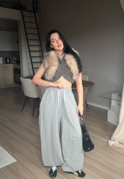 Pantalones de chándal grises de pierna ancha con cordón, combinados con una blusa corta de color verde oliva que presenta un cuello de piel sintética. Bolsa tote negra y zapatillas.