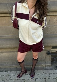 Balta josta aizdarāma sporta jaka ar bordo svītrām, kombinēta ar bordo šortiem. Caurskatāmas melnas ceļgalu augstuma zeķes un burgundijas sarkani papēži. Mazs rokassomiņa.