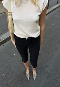 Ανοιχτό μπεζ ριγωτή μπλούζα, μαύρο εφαρμοστό παντελόνι μέχρι τον αστράγαλο και γκρι παπούτσια με αιχμηρή μύτη με τρία διακοσμητικά κουμπώματα. Τσάντα κρεμασμένη στον ώμο.