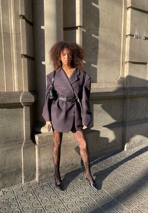 Blazer de gran tamaño en gris oscuro con líneas de hombros marcadas, ceñido a la cintura; combinado con medias de encaje y tacones negros.