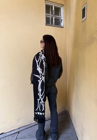 Must sall sallavalge abstraktse mustriga ja tuttidega, heidetud üle musta jope ja tumedate teksadega inimese õla.