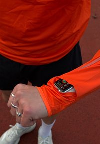 Jasnopomarańczowa, lekka koszula z długim rękawem, z dopasowanym rękawem z wycięciem na urządzenie elektroniczne lub zegarek.