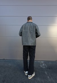 Hall gris oversized jakker, mustad cargo püksid ja rohelised/valged tossud, vaadatud selja tagant halli seina ees.