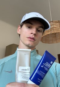 Twee huidverzorgingsproducten vastgehouden in de hand: een witte tube met het label "The Ordinary" en een blauwe tube met het label "Skin Fit Sun Cream", beide met gladde oppervlakken.