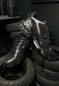 Zapatillas deportivas negras con una parte superior de malla, acentos sintéticos y amortiguación de aire visible. Presenta superficies texturizadas y suelas redondeadas.