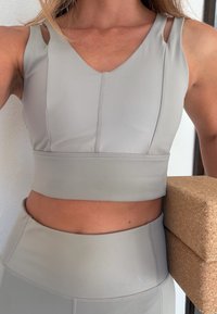 Szary sportowy top crop z dekoltem w serek, szerokimi ramiączkami i płaskimi szwami, zestawiony z dopasowanymi, wysokim stanem legginsami z gładkiej tkaniny.