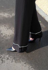 As calças largas pretas apresentam um acabamento em branco contrastante na bainha. Combinadas com sapatos de salto alto pretos de bico fino sobre uma superfície texturizada.