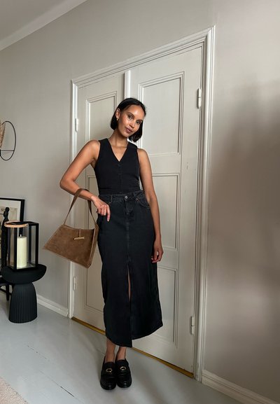 Top negro sin mangas con botones, falda de mezclilla negra de cintura alta con una abertura frontal, bolso de ante marrón y zapatos de plataforma negros con detalles dorados.